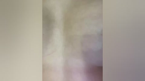 A blurry, indistinct video featuring a person in a white shirt, standing against a pale, off-white wall. The image lacks clarity, making it difficult to discern facial features or body details.