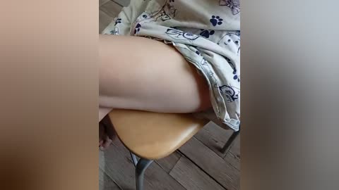 A video showing a light-skinned person's lower body and thighs, partially covered by a patterned white pajama bottom. The setting appears to be a wooden floor with a chair visible.
