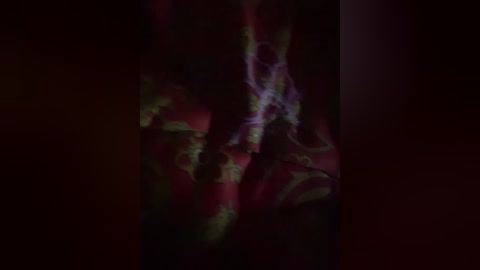 A dimly lit, abstract video features swirling, organic patterns in reds, greens, and purples, creating a mesmerizing, almost hypnotic effect. The image is blurred, emphasizing texture and movement over specific details.