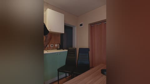 A video of a small, dimly lit kitchen with a green and white color scheme, featuring a black chair and wooden table, beige walls, and a closed orange curtain.