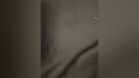 A blurry, dimly lit video of a dark-skinned person with a broad nose and thick lips, likely a male, partially visible against a greyish background. The image lacks distinct details and is poorly focused.