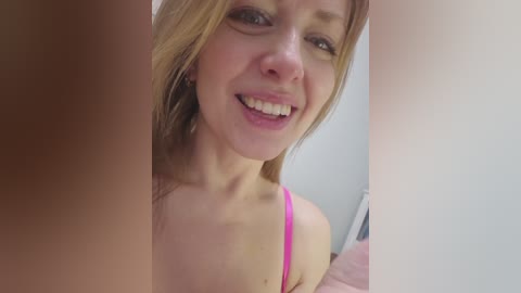 A video of a smiling, fair-skinned woman with light brown hair, wearing a pink bra, partially cropped.