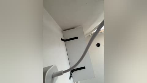 Video of a narrow, white-walled interior staircase with a gray handrail and black wall-mounted railings. A small window with a metal frame is visible at the top right. The scene is dimly lit, creating a minimalist, clean aesthetic.