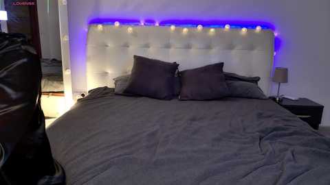 Video of a modern bedroom with a tufted white headboard, dark gray bedding, and purple LED strip lighting.