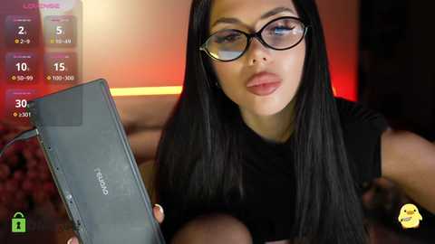 Video of a woman with long black hair, wearing black-rimmed glasses and a sleeveless black top, holding a black Acer laptop, with a blurred background showing a sports bar screen displaying game statistics.