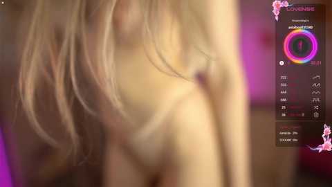 A blurred video of a nude blonde woman, likely in a bedroom, with a colorful virtual reality display in the background.