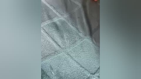 A close-up video of a grey, textured towel with a diamond pattern, featuring a faint, blurred image of a person's hand and fingers, possibly holding the towel.