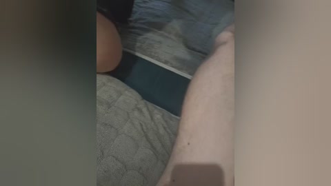 Video of a person lying on a bed, with a visible leg and thigh. The bed has a grey, quilted comforter. The person's skin tone is light.