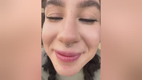 Close-up video of a young woman with fair skin, dark hair, and a nose ring, smiling widely. Background is blurred.