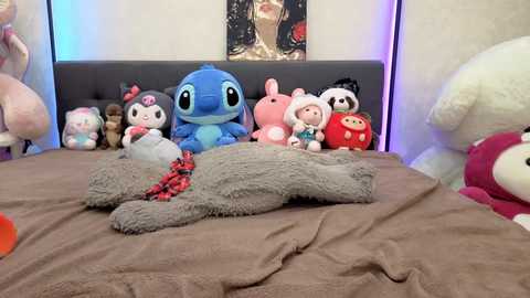 Video of a plush toy-filled bed with a blue alien, a red dragon, and a pink rabbit, set against a purple-lit wall with a framed picture.
