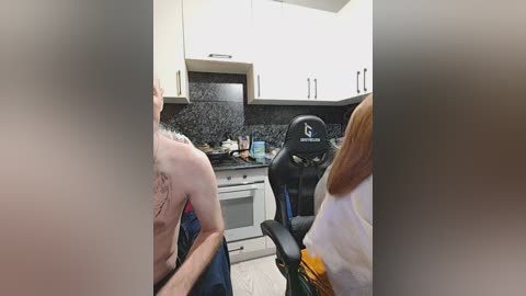 Video of a modern kitchen with a black granite countertop, white cabinets, and a gaming chair with a white shirt.