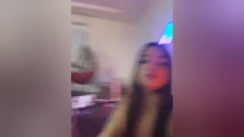 Blurry photo of a woman with long brown hair, smiling, wearing a dark top, in a dimly lit room with a colorful light on the wall.