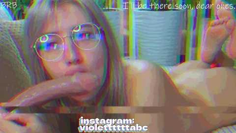 A digitally altered video features a young woman with light skin and glasses, lying on a bed with a large, erect penis inserted into her mouth. The background has colorful, abstract shapes. Text overlay reads \"Instagram: violettittab.\