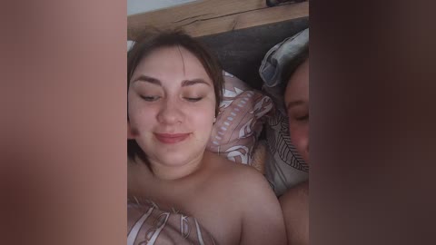 A candid video of a smiling woman with light skin and brown hair lying on a bed with patterned pillows, partially obscured by another person's arm.
