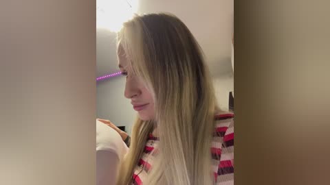 Video of a young Caucasian woman with long, straight, blonde hair, wearing a striped sweater, looking down in a dimly lit room with soft purple LED lights.