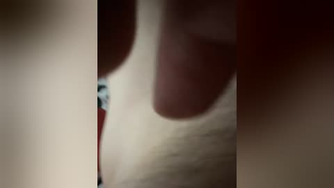 A blurred video of a person's hand with a red nail polish, holding a red object, possibly a lipstick. The background is out of focus, showing a beige surface.