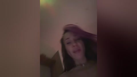 Blurry video of a woman with long dark hair, holding her hair back with one hand, in a dimly lit room.