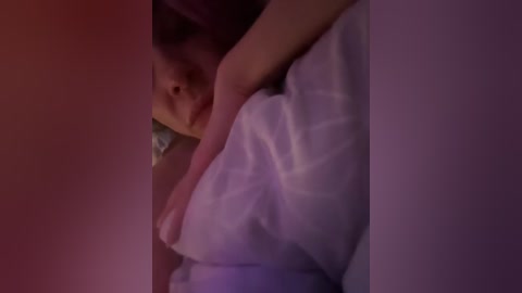 Video of a person with light skin, wearing a white shirt, lying in bed, head slightly tilted, with a soft, dim light casting a purple hue, creating a moody, intimate atmosphere.