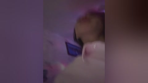 A blurry, out-of-focus video showing a close-up of a person with purple hair, possibly wearing a dark shirt, in a dimly lit room. The image is grainy, making it difficult to discern specific details.