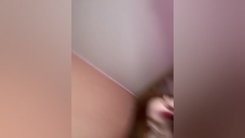 A blurred close-up video of a person's face with visible nose and lips, partially obscured by soft, pinkish-white light.