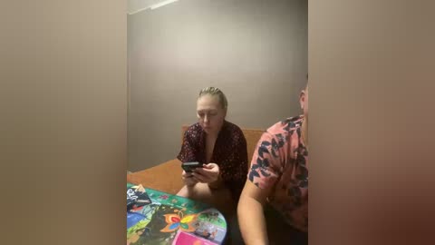 Video of a young blonde woman in a patterned shirt, sitting on a couch, focused on a tablet, surrounded by colorful blankets and a tiger-print shirt.