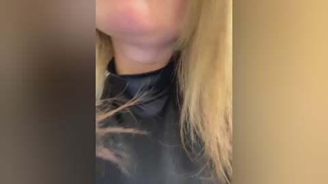 Video of a woman with long blonde hair wearing a black leather jacket, partially obscured by a beige wall. Her face is blurred.