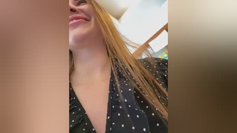 A close-up video of a young woman with fair skin and long, wet, light brown hair, smiling, wearing a black dress with white polka dots.