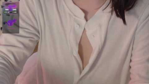 A close-up video of a person's upper body wearing a white button-up shirt, partially unbuttoned, revealing a hint of cleavage. The background is blurred, and the image has a soft, slightly grainy texture.