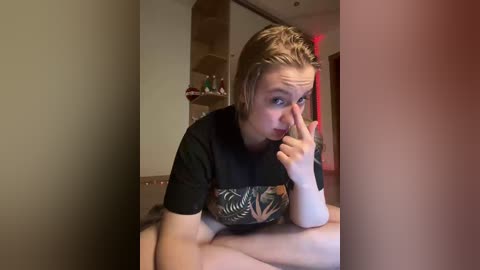 Video of a young woman with wet hair, wearing a black graphic T-shirt, sitting on a bed, making a peace sign with her fingers, in a dimly lit room with a wooden shelf and a red light in the background.