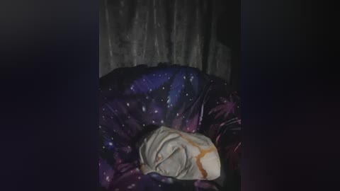 A video of a dark, textured fabric background with a small, folded, light-colored fabric item, possibly a blanket, with a hint of orange, lying on it.
