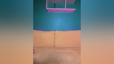 Video of a minimalist room with a beige couch, teal walls, and a small pink floating shelf with a doll.