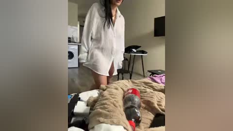 Video of a woman in a white shirt, kneeling next to a large, plush dog toy resembling a red and black rocket. Background includes a washer and dryer, a desk, and a TV.