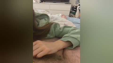 Video of a woman lying on a bed, wearing a green sweater, with a hand resting on her stomach, in a dimly lit bedroom.
