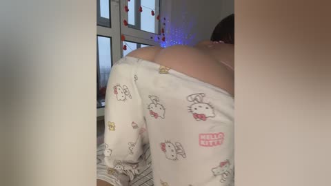Video of a woman in white Hello Kitty pajamas, with a prominent view of her bare backside, leaning against a window with red heart decorations.