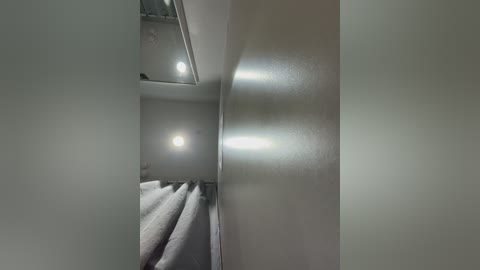 Video of a minimalist, modern bathroom with white walls and a large mirror reflecting a neatly folded towel. The room has a clean, uncluttered aesthetic with soft lighting from a recessed ceiling fixture.