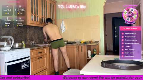 Video of a shirtless man in green boxer briefs, cooking in a modern kitchen, with a fitness app overlay showing stats and workout options.