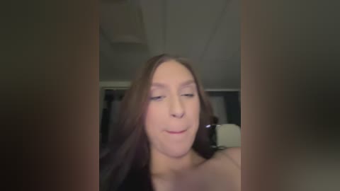 Video of a young woman with long brown hair, closed eyes, and a slight smile, taken indoors with dim lighting, showing a blurred background and two vertical lines obscuring the top and bottom of the image.