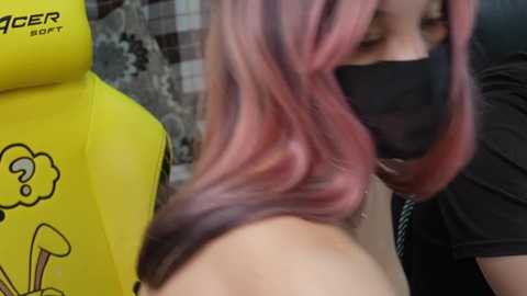 Video of a person with pink and purple hair wearing a black mask and a yellow gaming chair with SpongeBob cartoon character.
