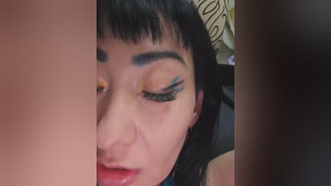 Close-up video of an Asian woman with short black hair, wearing heavy black eyeliner and eyeshadow. She has a relaxed expression, slightly smiling with closed eyes, in a dimly lit room with a patterned pillow.