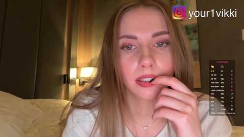 Video of a young Caucasian woman with long blonde hair, light skin, and light makeup, holding her finger to her lips in a bedroom setting.