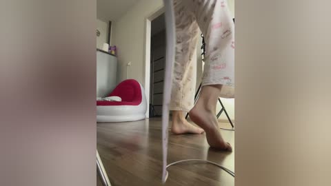 Video of a child in pajamas walking barefoot on a wooden floor, with a red beanbag chair and white wall in the background.