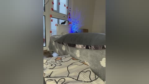Video of a cozy bedroom with a bed covered in a gray duvet featuring white cloud designs. A fluffy cat lounges on the floor, and a radiant blue light illuminates the room.