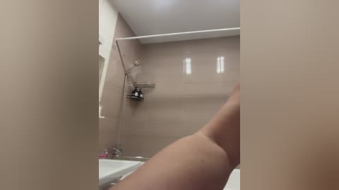 Video of a beige-tiled bathroom with a white bathtub and a person's lower leg and foot visible, partially obscured by the frame.