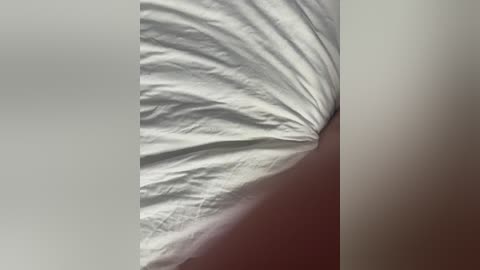 A video captures the crumpled, wrinkled corner of a white bedsheet, creating a textured, ridged pattern. The background is a muted, gradient beige, adding contrast to the crisp, clean sheet.