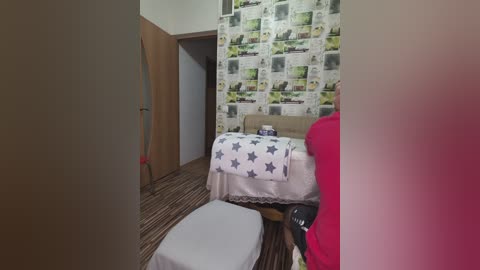 A video of a small, neatly arranged bedroom with a bed covered in a star-patterned comforter, a pink chair, and a striped carpet. The walls are adorned with newspaper clippings.