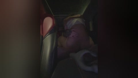 A dimly lit video shows a person lying on a bus seat, partially hidden by a red and white heart-shaped pillow, with a beige blanket covering their head. The background is dark, and the image has a moody, intimate atmosphere.