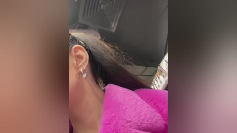 A video of a person's head with shoulder-length brown hair, wearing a pink towel and silver earrings, lying on a bed with a gray ceiling fan visible.