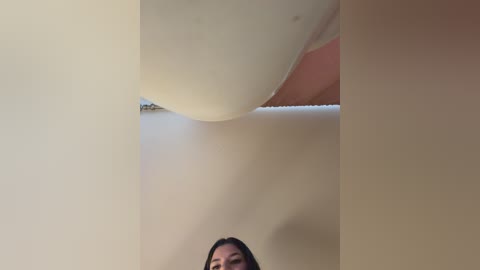 A video of a ceiling with a light fixture, a woman's face partially visible at the bottom, her hair dark and long. The ceiling is painted a neutral beige.