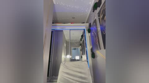 Video of a narrow, dimly lit hallway with white walls, a reflective glass door, and a white bed covered in a blanket at the end. Decorations include green and red balloons.