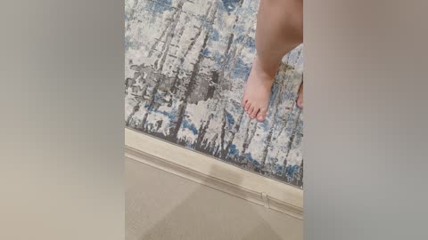 Video of a person's bare feet on a beige tiled floor, standing on a blue and white abstract forest-themed rug with a textured finish.